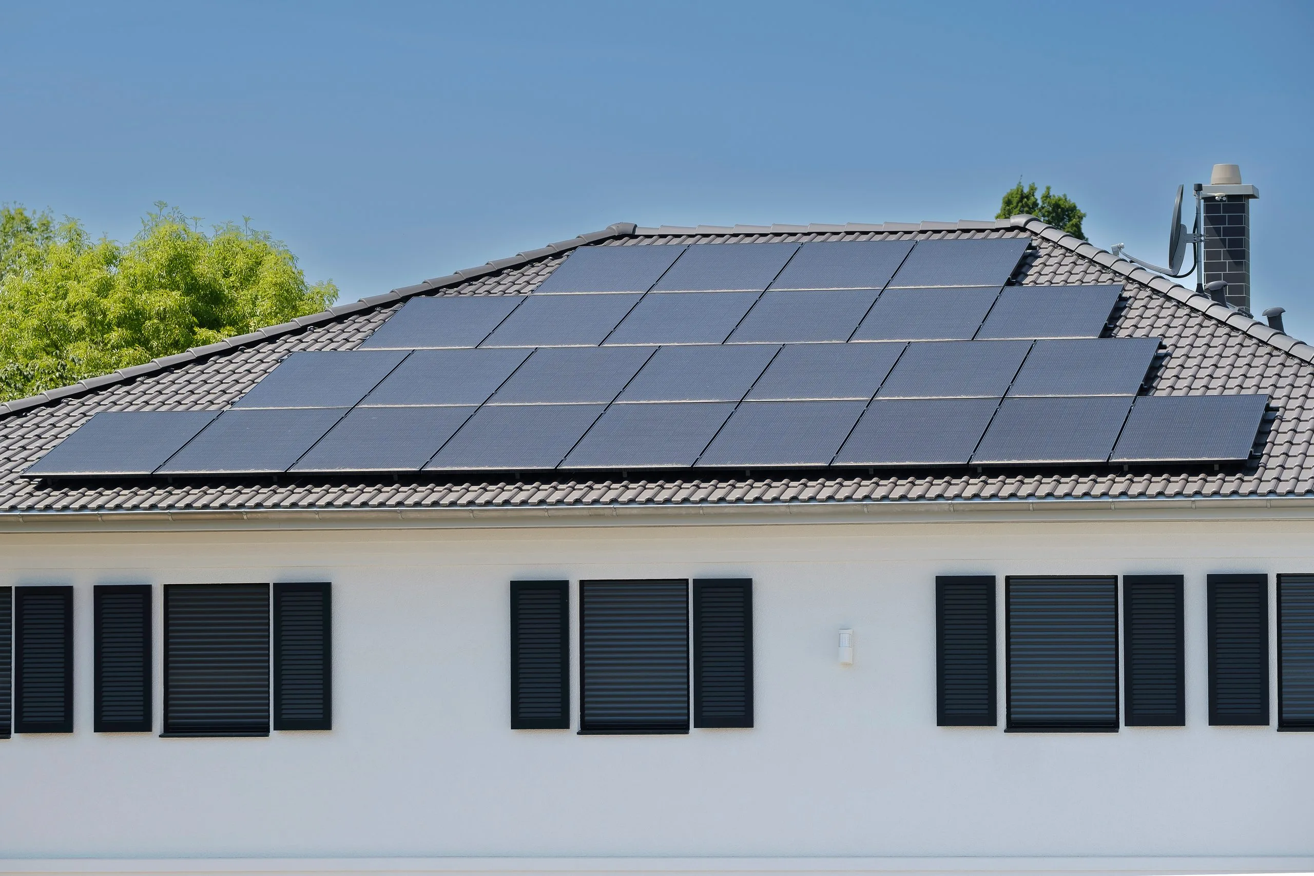 Steildach mit Ziegeleindeckung und aufgesetzter Photovoltaik-Anlage in der Sommersonne.