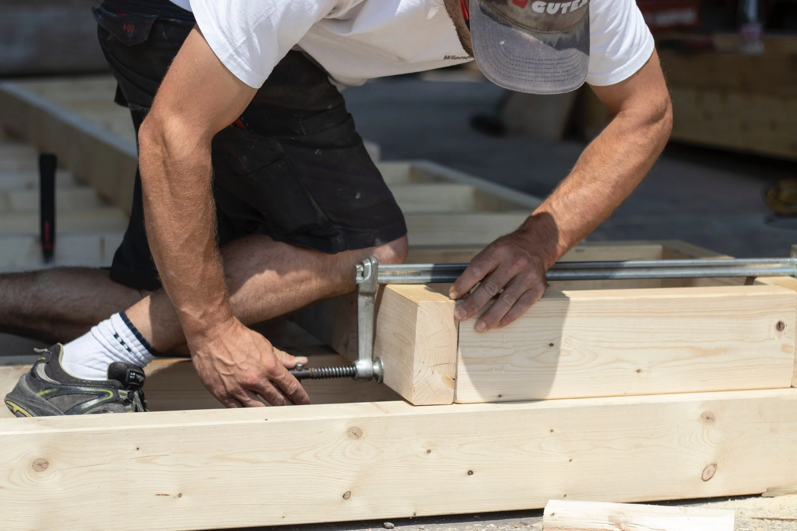 Zimmerer verschraubt und verspannt Holzbalken mit Schraubzwinge auf einer Baustelle.