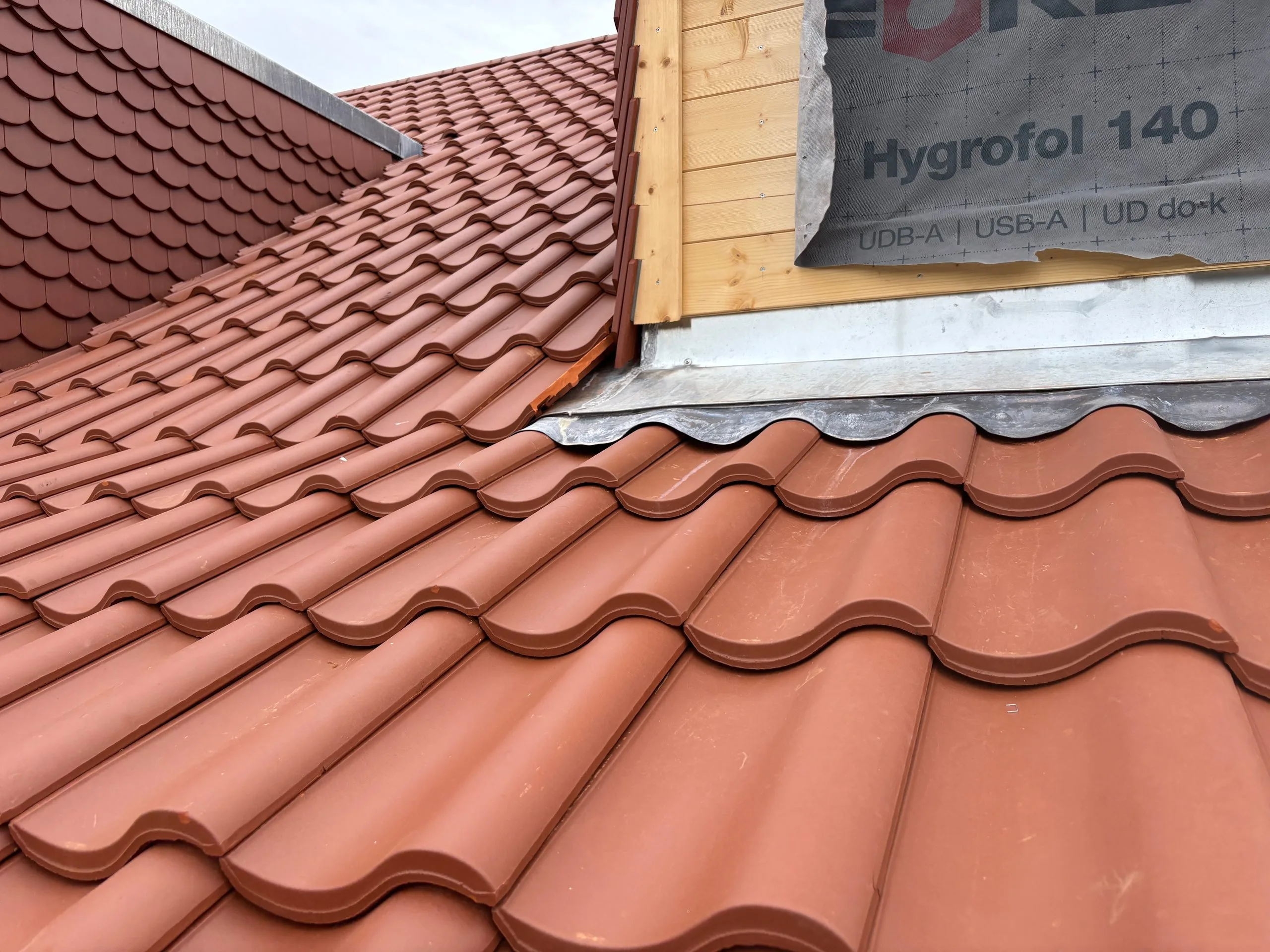 Frisch verlegtes Tondachziegel-Dach mit sauberem Blechanschluss an der Gaubenwand.
