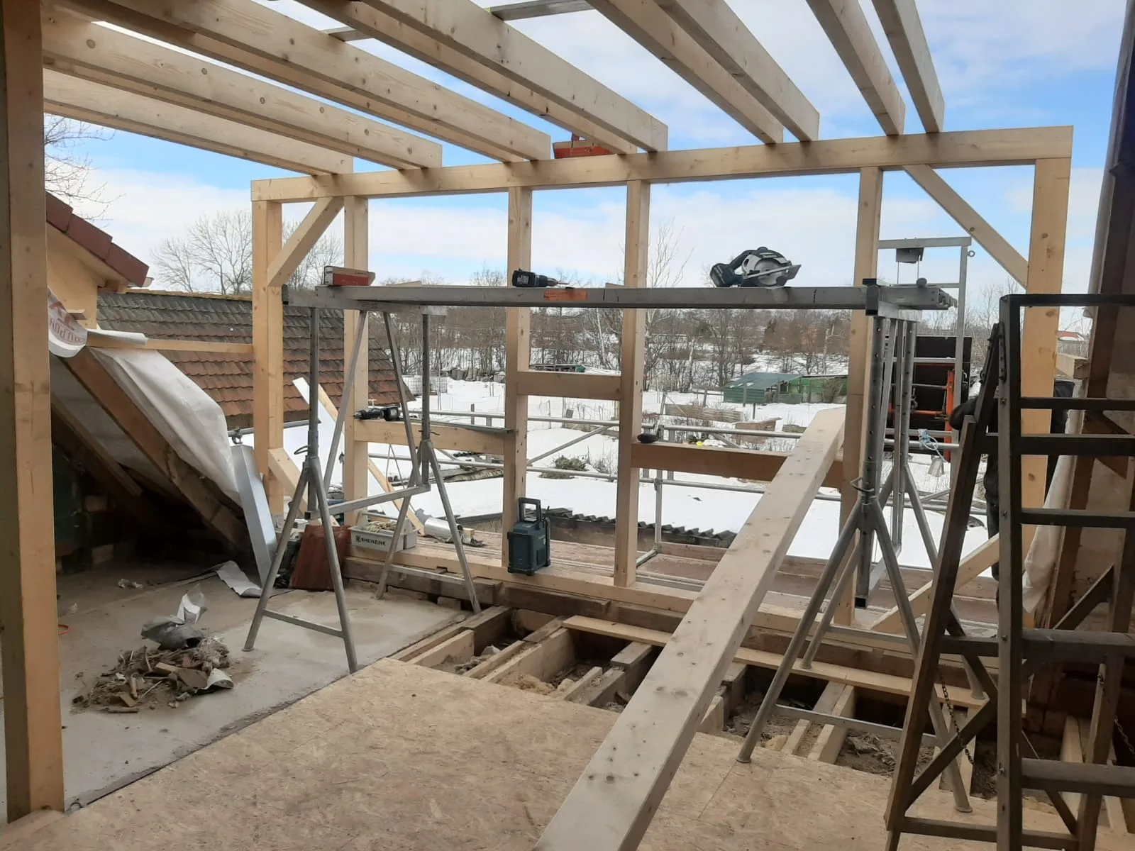 Neu errichtetes Holztragwerk für einen Dachstuhl mit Sparren und Pfetten über verschneiter Landschaft.