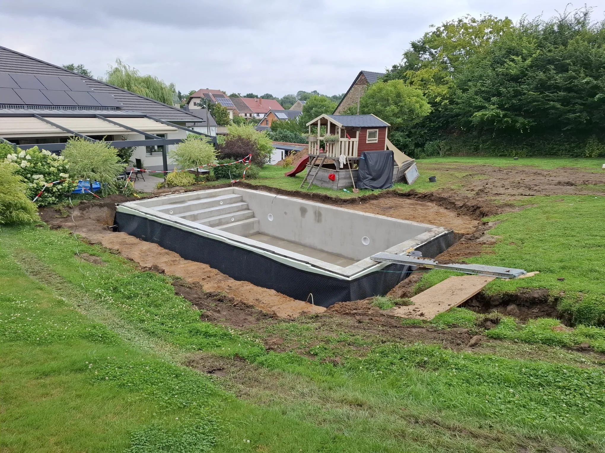 Frisch eingebautes Poolbecken im Garten mit umliegendem Erdaushub.