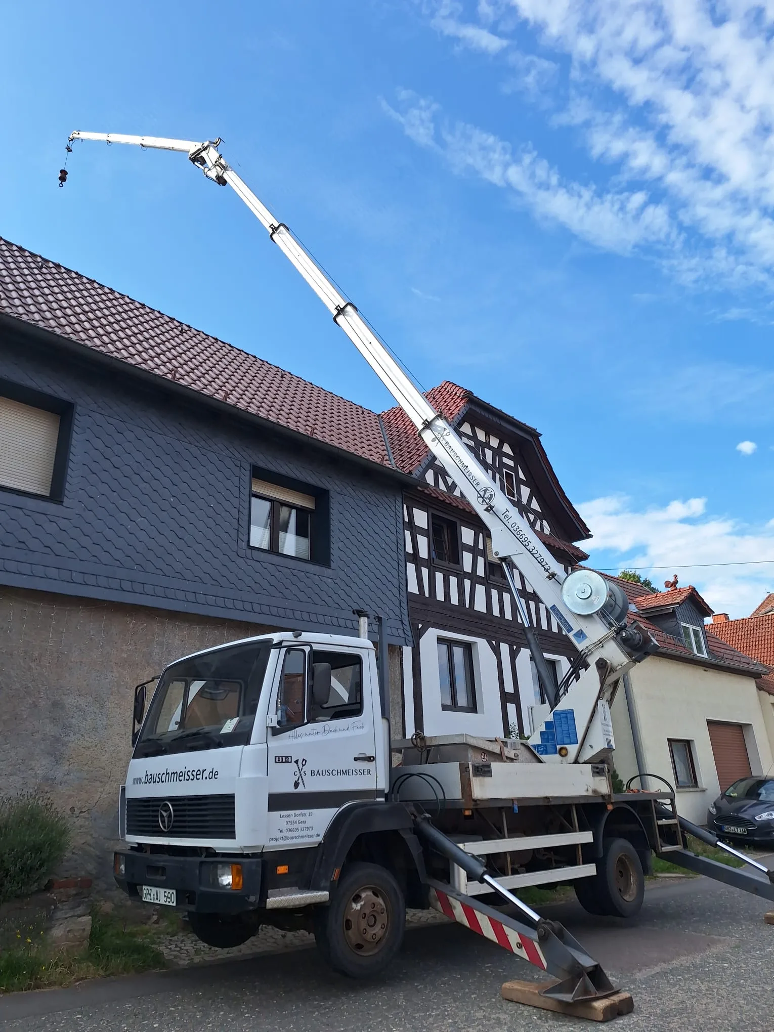 LKW-Kran von Bauschmeisser vor einem sanierten Fachwerkhaus mit dunkler Schieferverkleidung.