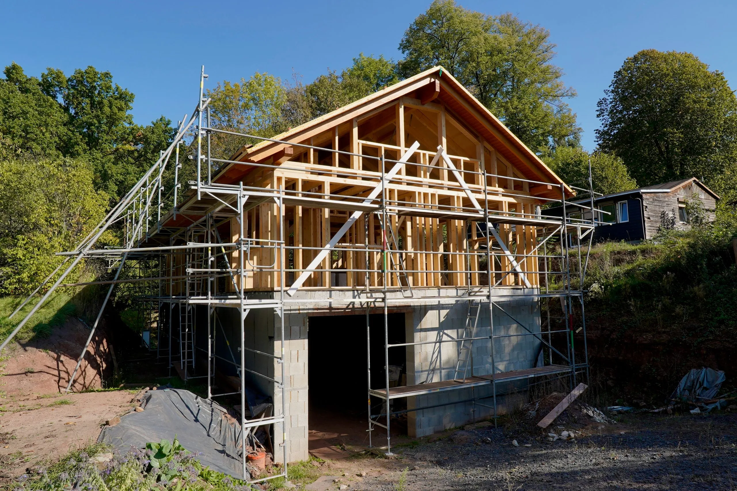 Holzrahmenbau mit Satteldach im Rohbau, umgeben von einem Metallgerüst.